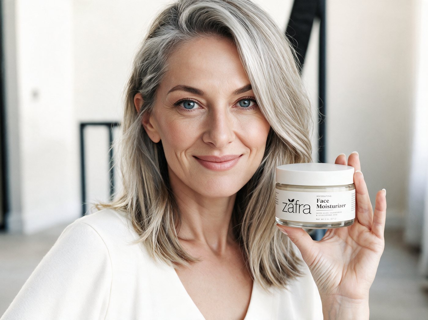 Smiling woman with silver hair holding the Zafra moisturizer jar